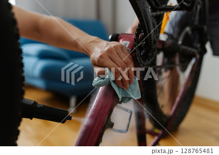Close-up of bike mechanic cleaning bicycle frame with water sprayer and cloth, focusing on thorough maintenance and hygiene in workshop environment. Concept of bicycle service. 128765481