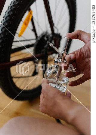 Close-up of cyclist spraying bicycle wheels with water, cleaning spokes and rims, performing detailed maintenance for peak cycling performance and equipment care at home. Concept of bike service. Close-up of cyclist spraying bicycle wheels with water, cleaning spokes and rims, performing detailed maintenance for peak cycling performance and equipment care at home. Concept of bike service. 128765482