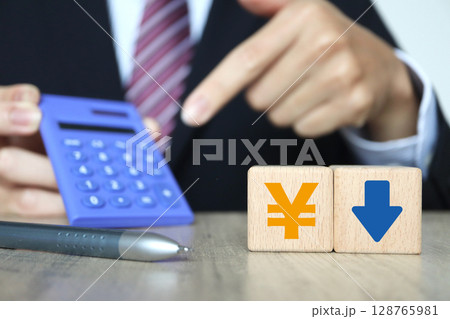 ビジネスマンと電卓。日本円記号と下向き矢印。 ビジネスマンと電卓。日本円記号と下向き矢印。 128765981
