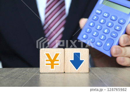 ビジネスマンと電卓。日本円記号と下向き矢印。 ビジネスマンと電卓。日本円記号と下向き矢印。 128765982