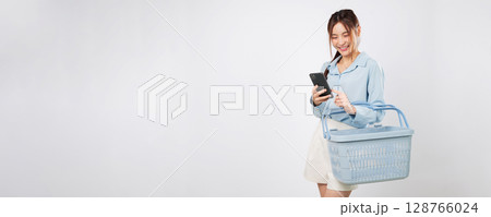 Basket in hand, shopping Asian woman holding mobile phone at supermarket shopping checklist shows online grocery convenience and happy lifestyle. isolated studio white background Basket in hand, shopping Asian woman holding mobile phone at supermarket shopping checklist shows online grocery convenience and happy lifestyle. isolated studio white background 128766024