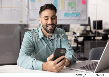 Happy Hispanic businessman using his smartphone in modern workplace Happy Hispanic businessman using his smartphone in modern workplace 128767018