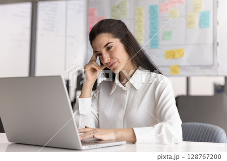 Woman review new software on laptop seated at desk Woman review new software on laptop seated at desk 128767200