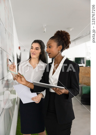 Two multiethnic women colleagues make data analysis, develop marketing strategy 128767206