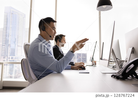 Callcenter male agent wear headset talking to client using computer Callcenter male agent wear headset talking to client using computer 128767224