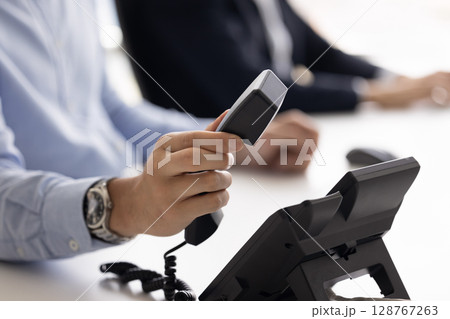 Closeup male hand holding telephone receiver, answers or ending phonecall Closeup male hand holding telephone receiver, answers or ending phonecall 128767263