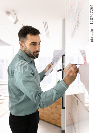 Hispanic man holds papers, writing information on whiteboard 128767264