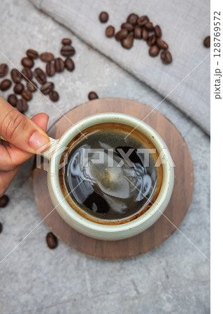 Shot from a bird eye view, a steaming cup of black coffee is held gently over a stone tabletop at a cafe. Shot from a bird eye view, a steaming cup of black coffee is held gently over a stone tabletop at a cafe. 128769572