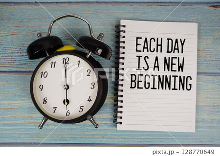 Each day is a New Beginning text written on notepad with alarm clock on wooden background 128770649