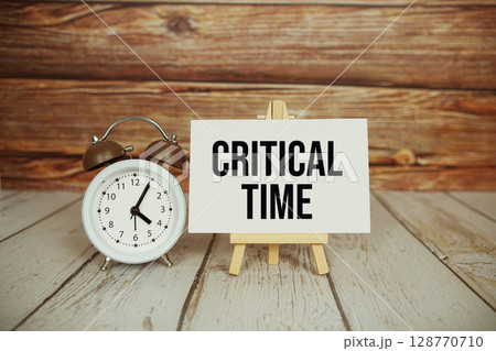 Critical Time text with easel and alarm clock on wooden background 128770710