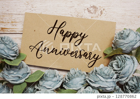 Happy Anniversary text on paper card with rose flowers bouquet on wooden background 128770862