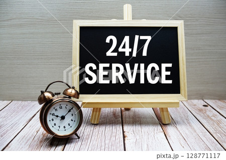 24 Hrs 7 Days Service text written on chalkboard with alarm clock on wooden background 128771117