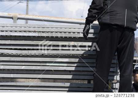 足場の組み立て　資材をトラックから降ろして準備する職人 128771238