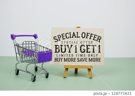 Buy 1 Get 1 Special Offer text with mini trolley shopping cart on green background Buy 1 Get 1 Special Offer text with mini trolley shopping cart on green background 128771621