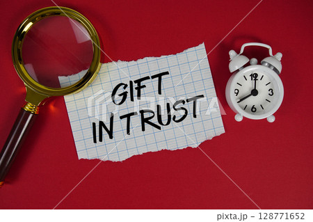 Gift In Trust text written on paper with magnifying glass and alarm clock 128771652