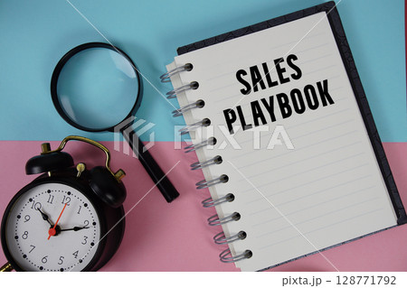 Sales Playbook text written on notebook paper with magnifying glass and alarm clock Sales Playbook text written on notebook paper with magnifying glass and alarm clock 128771792