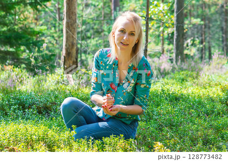 Blonde woman collecting cranberries in forest Blonde woman collecting cranberries in forest 128773482