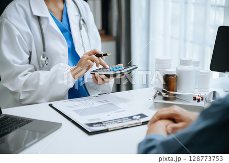 Healthcare costs and fees concept.Hand of smart doctor used a calculator and smartphone, tablet for medical costs at hospital Healthcare costs and fees concept.Hand of smart doctor used a calculator and smartphone, tablet for medical costs at hospital 128773753