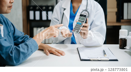 Healthcare costs and fees concept.Hand of smart doctor used a calculator and smartphone, tablet for medical costs at hospital Healthcare costs and fees concept.Hand of smart doctor used a calculator and smartphone, tablet for medical costs at hospital 128773801