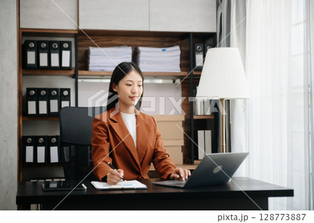 Young beautiful woman typing on tablet and laptop while sitting at the working wooden table modern office 128773887