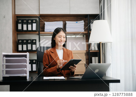 Young beautiful woman typing on tablet and laptop while sitting at the working wooden table modern office 128773888