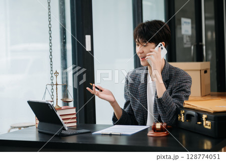 Asian female lawyer chatting online with client on laptop, smartphone discussing details of lawsuit. in modern office Asian female lawyer chatting online with client on laptop, smartphone discussing details of lawsuit. in modern office 128774051