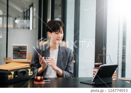 Asian female lawyer chatting online with client on laptop, smartphone  discussing details of lawsuit. in modern office 128774053