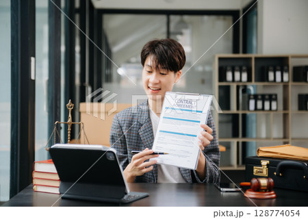 Asian female lawyer chatting online with client on laptop, smartphone  discussing details of lawsuit. in modern office 128774054