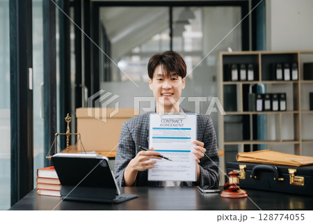 Asian female lawyer chatting online with client on laptop, smartphone  discussing details of lawsuit. in modern office 128774055