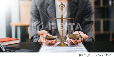Male lawyer in the office with brass scale on wooden table. justice and law concept in morning light Male lawyer in the office with brass scale on wooden table. justice and law concept in morning light 128774102
