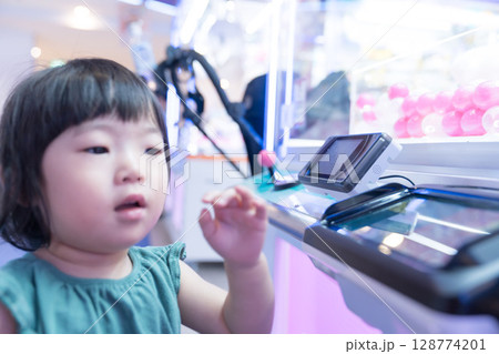 ゲームセンターのUFOキャッチャーで遊ぶ女の子の幼児 ゲームセンターのUFOキャッチャーで遊ぶ女の子の幼児 128774201