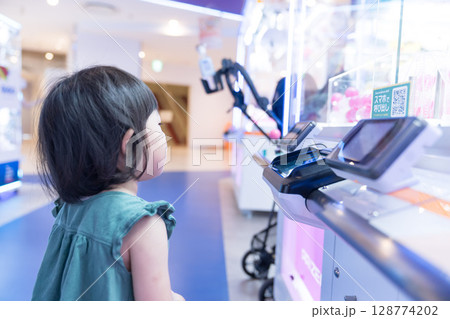 ゲームセンターのUFOキャッチャーで遊ぶ女の子の幼児 ゲームセンターのUFOキャッチャーで遊ぶ女の子の幼児 128774202