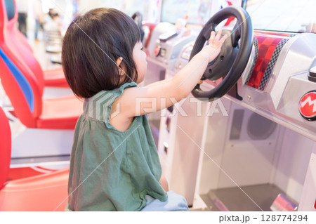 ゲームセンターのレーシングゲームで遊ぶ女の子の幼児 ゲームセンターのレーシングゲームで遊ぶ女の子の幼児 128774294