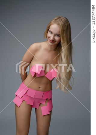 Blonde woman in a studio wearing a creative outfit made of pink sticky notes 128774494