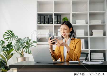 Confident Asian woman with a smile standing holding notepad and tablet at the office. 128774561