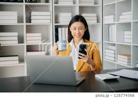 Confident Asian woman with a smile standing holding notepad and tablet at the office. 128774566