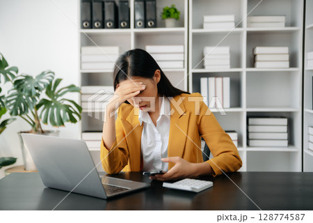 Asian woman feeling migraine head strain.Overworked businesswoman financier while working on laptop and tablet at office. Asian woman feeling migraine head strain.Overworked businesswoman financier while working on laptop and tablet at office. 128774587