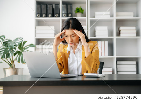Asian woman feeling migraine head strain.Overworked businesswoman financier while working on laptop and tablet at office. Asian woman feeling migraine head strain.Overworked businesswoman financier while working on laptop and tablet at office. 128774590