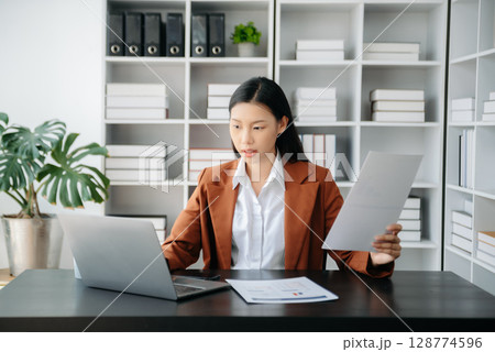 Beautiful Asian business woman typing laptop and tablet Placed at the table at the office Beautiful Asian business woman typing laptop and tablet Placed at the table at the office 128774596