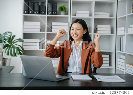 Asian business woman are delighted and happy with the work they do on their tablet, laptop and taking notes at office. 128774862