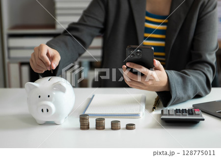 Business woman hand putting money coin into piggy bank with step of growing stack coins for saving money with virtual icon Business woman hand putting money coin into piggy bank with step of growing stack coins for saving money with virtual icon 128775011