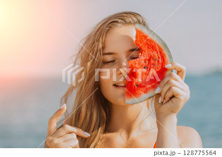 Watermelon Beach Summer: Woman playfully holds watermelon slice, covering face, enjoying sunny beach day. Watermelon Beach Summer: Woman playfully holds watermelon slice, covering face, enjoying sunny beach day. 128775564