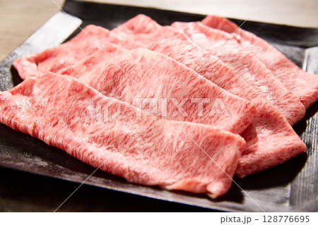 黒毛和牛の霜降りスライス肉を黒い角皿に美しく盛り付けたクローズアップ写真。艶やかな脂と繊細なサシ模様 128776695