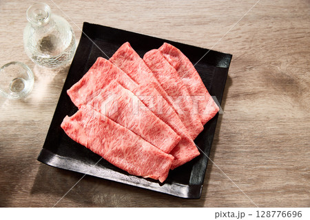 黒毛和牛の霜降りスライスを黒い角皿に整然と並べ、日本酒の徳利と盃を添えた、真俯瞰構図による高級和食 黒毛和牛の霜降りスライスを黒い角皿に整然と並べ、日本酒の徳利と盃を添えた、真俯瞰構図による高級和食 128776696