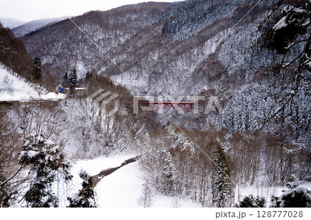 雪景色に映える赤い高井橋と山田温泉周辺の冬の渓谷風景（長野県） 128777028
