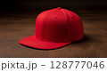 A vibrant red flat-brim baseball cap rests on a dark wooden surface. 128777046