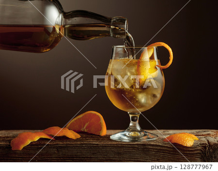 Old Fashioned cocktail with ice and orange peel on a old wooden table. Old Fashioned cocktail with ice and orange peel on a old wooden table. 128777967