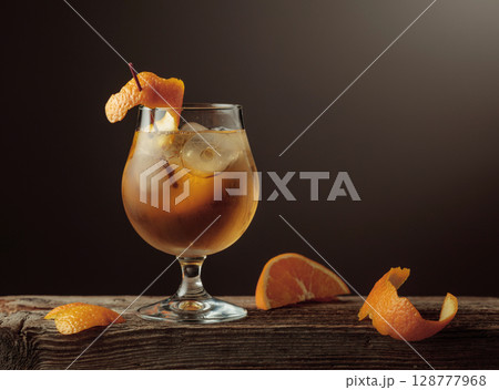 Old Fashioned cocktail with a ice, garnished with an orange peel on a old wooden board. Old Fashioned cocktail with a ice, garnished with an orange peel on a old wooden board. 128777968