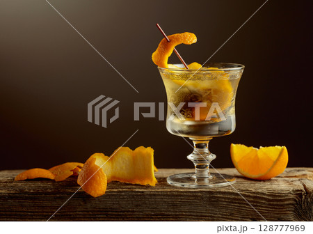 Old Fashioned cocktail with a ice, garnished with an orange peel on a old wooden board. Old Fashioned cocktail with a ice, garnished with an orange peel on a old wooden board. 128777969