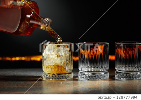 Whiskey is poured into a glass with ice. Whiskey is poured into a glass with ice. 128777994